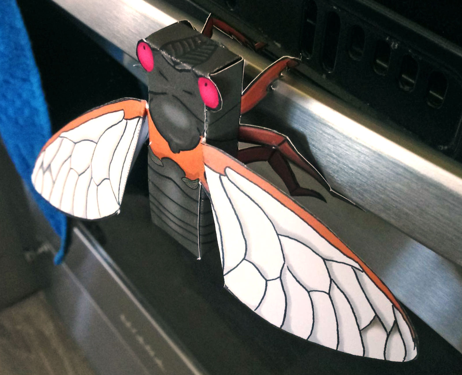 A cute papercraft cicada hangs from a stove handle